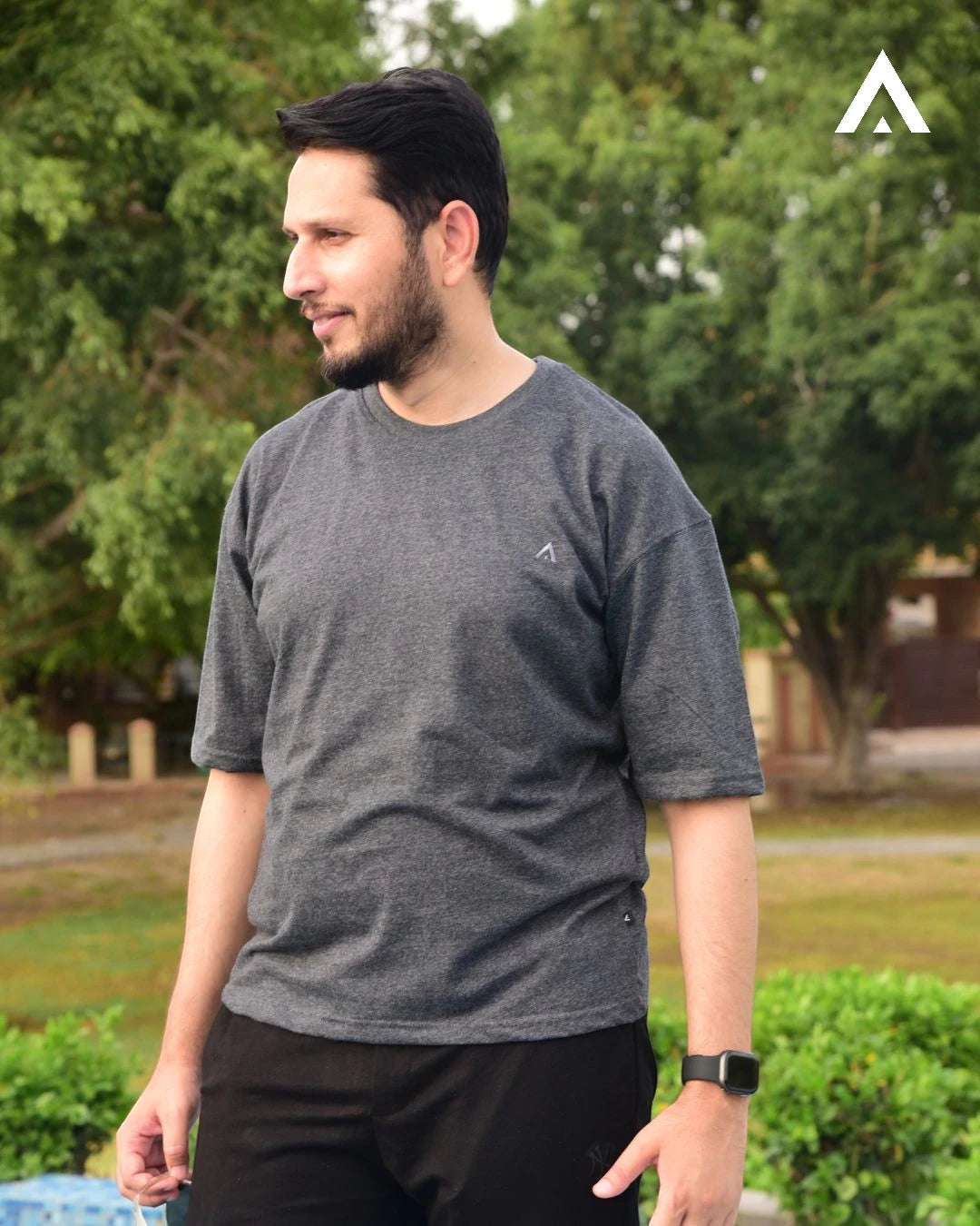 Man wearing a gray t-shirt with a logo outdoors