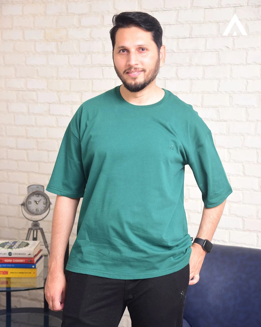Man wearing a green t-shirt standing against a white brick wall.