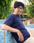 Man wearing glasses and a navy blue shirt sitting by a pool with greenery in the background