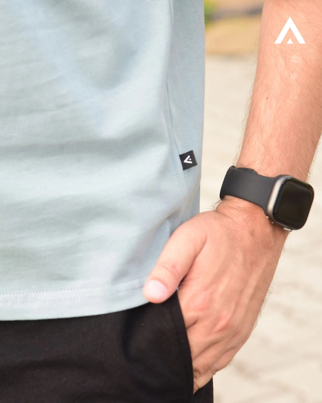 Person wearing a light blue shirt with a logo and a smartwatch on a blurred background